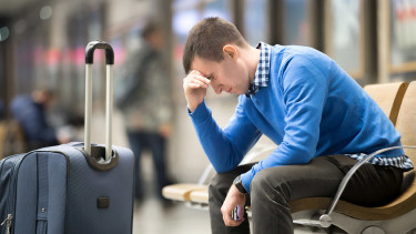 Urlauber sitzt mit Koffer nachdenklich am Flughafen